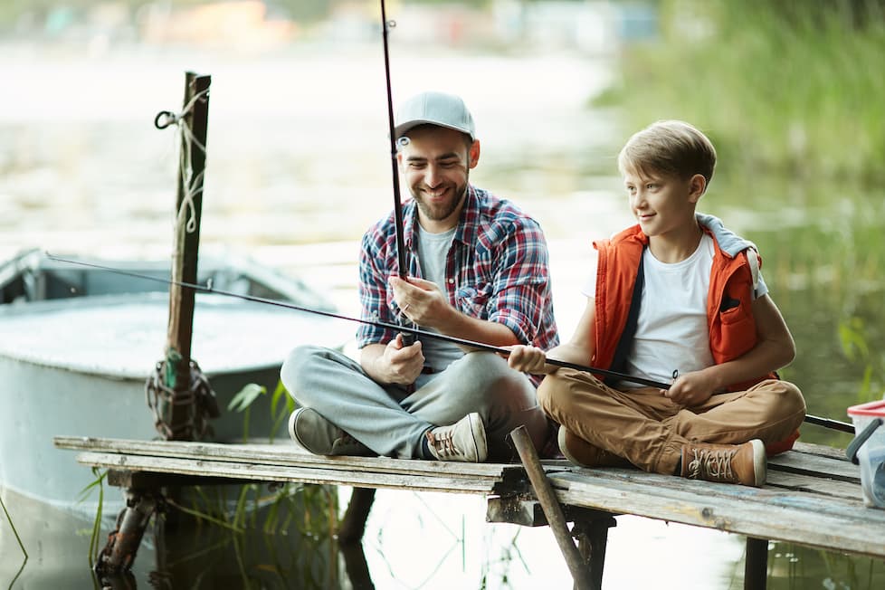 Father sitting on a dock fishing together.